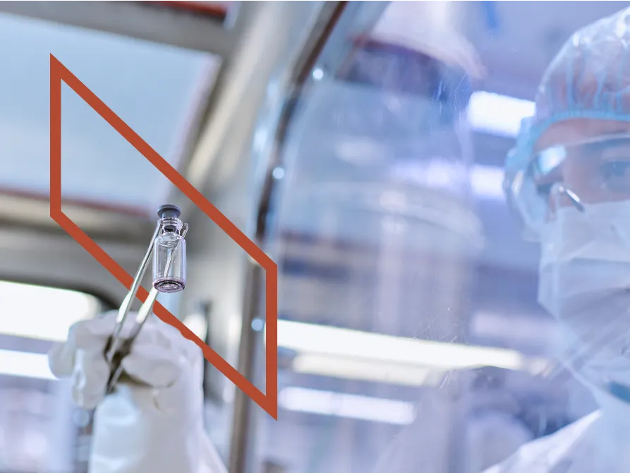 A scientist in protective gear holds a vial with forceps inside a laboratory cleanroom, seen through a glass barrier with a red outlined rectangle.